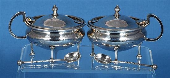 A pair of George V Arts & Crafts silver mustard pots with matching spoons, by Albert Edward Jones, width 90mm, weight 5.1oz/160grms.